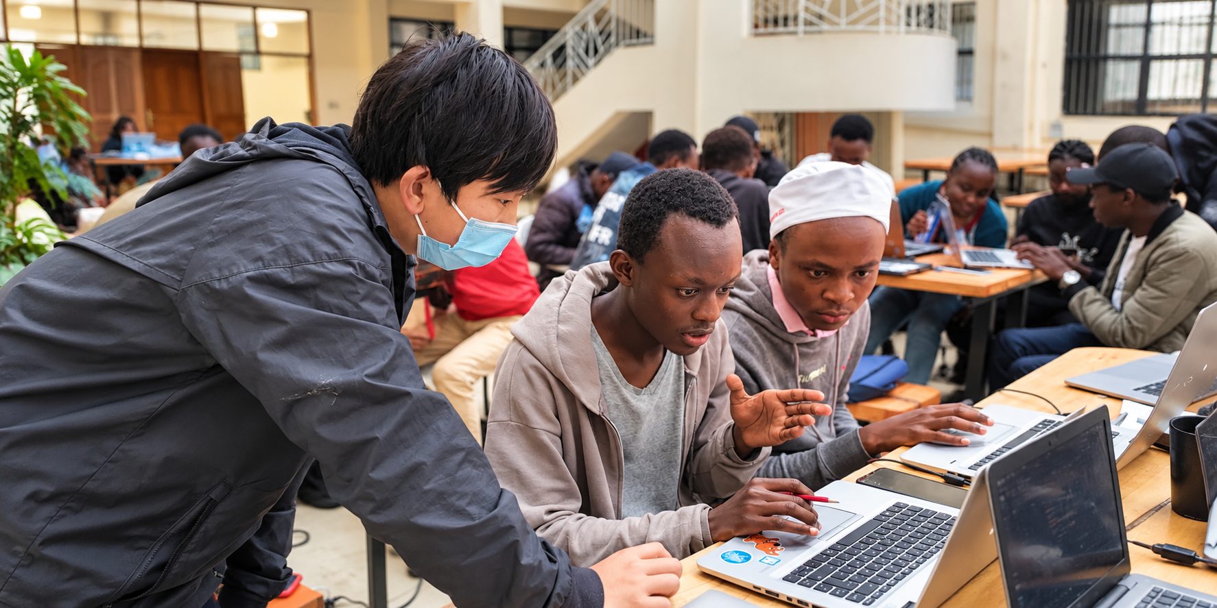 Arthur helping two students with code on their laptops in a busy study hall